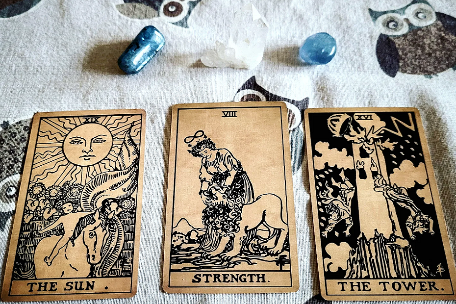 Tarot oplæg der viser The Sun, Strength og The Tower. Bagved er der to blå krystaller og en bjergkrystal.